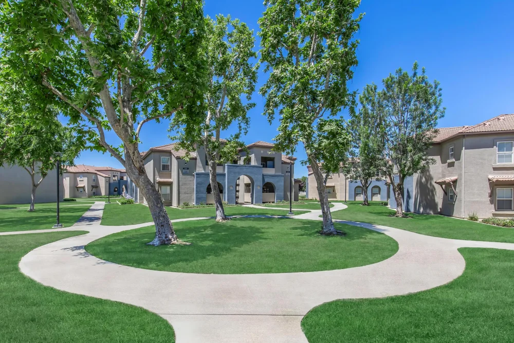 Apartment buildings arranged around a broad lawn with mature shade trees and curved paths.